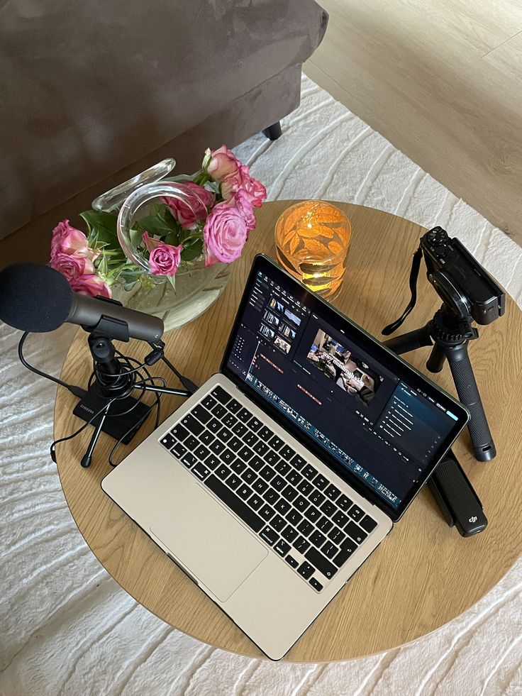 Macbook ouvert sur une page de montage video. Accompagner d'un micro, trepied et camera sur une table de salon